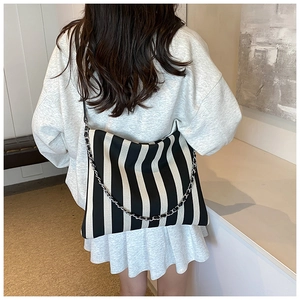 Lifestyle view of a black and white striped canvas tote bag with chain strap on shoulder