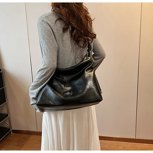 Detail of glossy wrinkled leather tote with knotted strap and metal logo plaque
