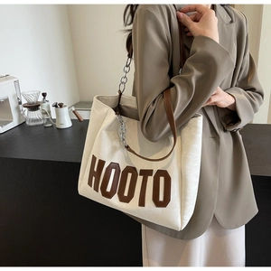Detailed view of cream tote bag with brown leather handles and decorative silver chain