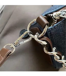 Détail du crochet et chaîne en argent sur sac en jean avec garniture en cuir marron
