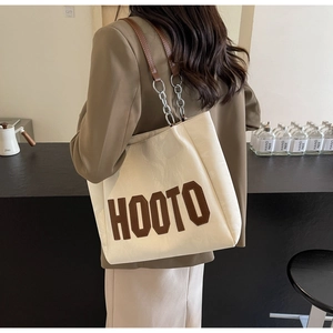 Detail of a beige tote bag with HOOTO logo and brown leather chain strap on a model