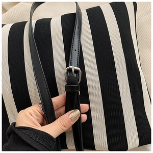 Detail of adjustable black leather strap and silver buckle on striped canvas bag