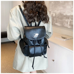 Detail of black pebbled leather backpack with silver B-logo and drawstring closure