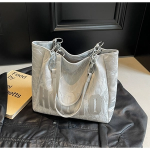 Detail of silver tote bag with crinkled texture, metal chain strap and HUOTO logo