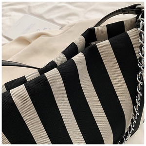 Detail of striped knit tote bag featuring black leather handle and silver metal chain strap