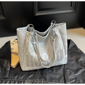 Detail of silver tote bag with HUOTO lettering and chain strap on leather background