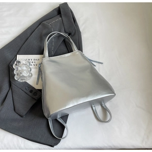 Chic silver tote bag with metallic finish shown in a stylish lifestyle setting on a bed