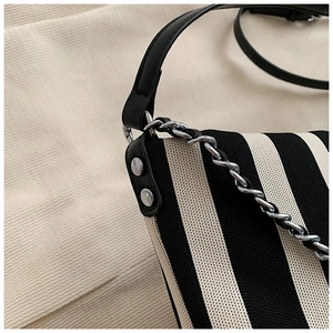 Detail of striped canvas bag featuring black leather strap and silver metal chain accessory