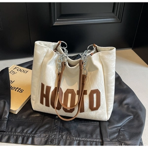 Detail of white pleated tote bag with HOOTO patch, brown leather strap, and silver chain
