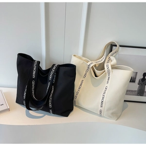 Detail of canvas tote bag showing black and white printed straps with logo text