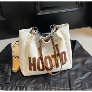 Detail of white tote bag with HOOTO brown leather patch and chain handle on leather jacket