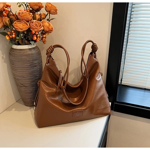 Macro shot of brown leather tote bag with unique knot detail and metallic logo plaque