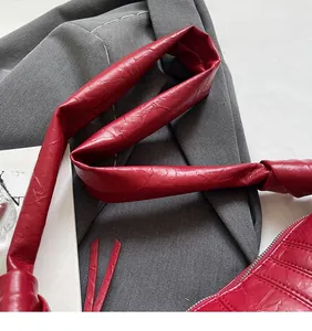 Close-up of red wrinkled leather texture with knotted shoulder strap on crescent bag