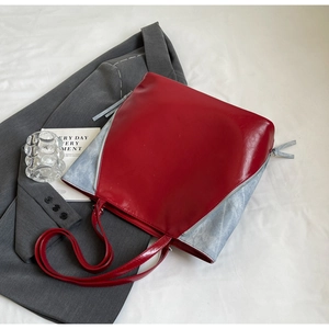 Detail of color-block tote bag with deep red glossy leather and grey textured side panels