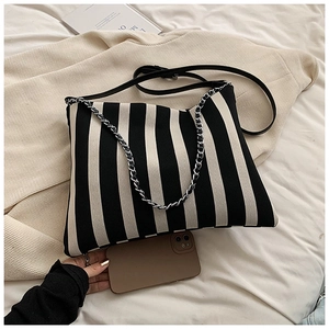 Detail of striped canvas tote bag with silver chain handle and leather strap on soft fabric