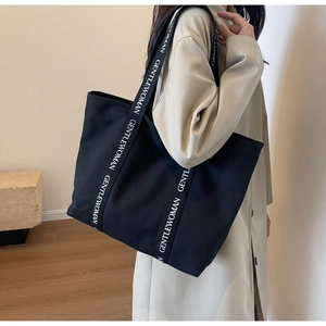 Close-up of black canvas tote bag with GENTLEWOMAN letter print wide shoulder strap