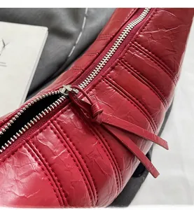 Detail of red crescent bag with quilted texture and smooth silver metal zipper closure
