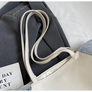 Detail of cream white faux leather tote with blue denim patchwork and long shoulder straps