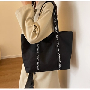 Detailed view of black canvas tote bag with Gentlewoman lettered straps on model's shoulder