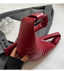 Macro detail of wine red crescent bag featuring pleated texture and knot handle detail
