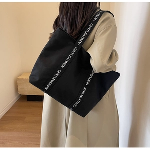 Detail of black canvas tote bag featuring white GENTLEWOMAN printed logo on wide strap
