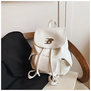 Detail of white textured leather backpack featuring gold B logo and drawstring closure