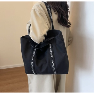 Detail of minimalist black canvas tote bag showing branded lettering on the woven handles