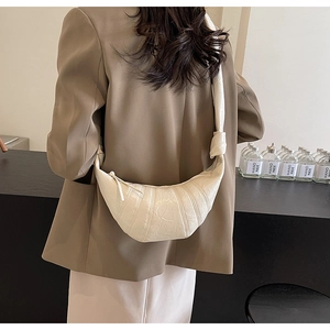 Detail of cream croissant shoulder bag with pleated texture and knot strap on shoulder