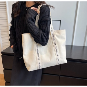 Detail of minimalist cream canvas tote bag featuring black GENTLEWOMAN lettered straps