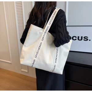 Detailed view of wide shoulder strap with black lettering on off-white canvas tote bag