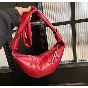 Detail of red croissant bag featuring glossy leather texture and stylish pleated stitching