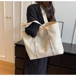 Side view of a large cream canvas tote bag with GENTLEWOMAN strap worn by a model