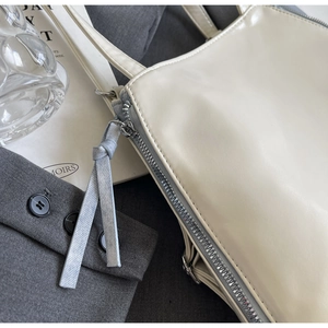 Detail of a minimalist off-white shoulder bag featuring a silver zipper and leather tassel
