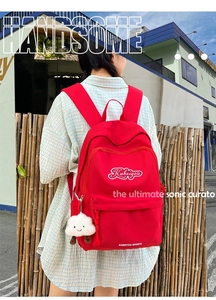 Dettaglio dello zaino in nylon rosso con ciondolo a nuvola e logo del marchio all'aperto