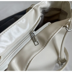 Detail of a beige PU leather tote showing silver metal zipper and smooth glossy finish