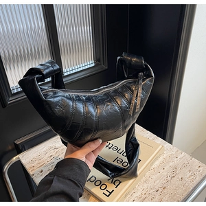 Detail of black crescent hobo bag featuring quilted texture and wide knotted shoulder strap