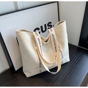 Detail of the woven strap with black lettering on a cream canvas tote bag