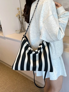Striped canvas shoulder bag with chain strap worn by a model in a minimalist home setting