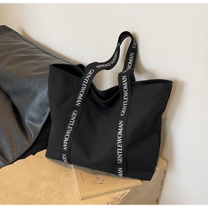 Detail of black canvas tote bag featuring white GENTLEWOMAN lettered shoulder strap