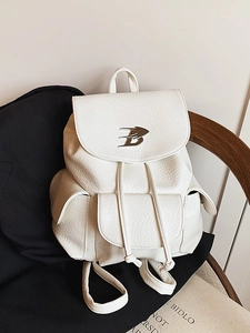 White faux leather backpack with metallic B-logo on black blazer and wooden chair