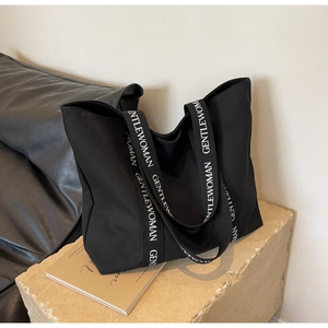 Detail of wide black canvas strap with white GENTLEWOMAN lettering on a tote bag