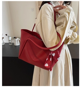 Detail of red pebbled leather tote bag featuring a decorative heart print scarf accessory