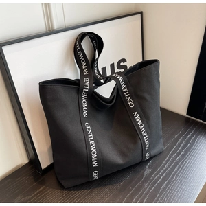Close-up of wide canvas shoulder strap with white Gentlewoman text on a black tote bag