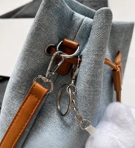 Detail of silver hardware and leather trim on light blue denim bucket bag with plush charm