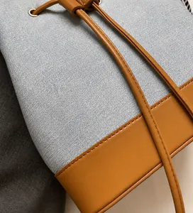 Detail of light blue denim bucket bag featuring brown faux leather trim and drawstring