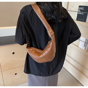 Brown pleated leather croissant bag with knotted wide strap shown in a lifestyle view