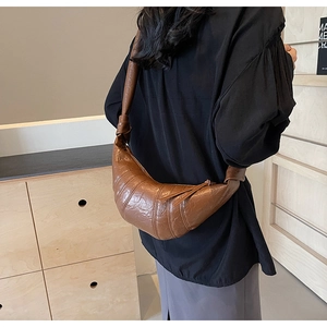 Detail of a dark brown pleated croissant bag with knotted shoulder strap on model