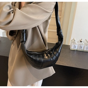 Detail of black croissant bag featuring knotted shoulder strap and textured leather finish