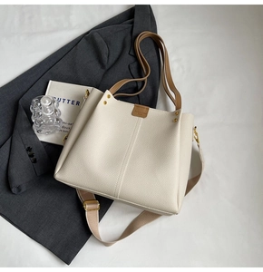 Detailed macro of cream-white lychee grain tote bag with brown leather handles and gold studs