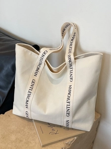 Minimalist off-white canvas tote bag with black lettered shoulder straps for daily commute